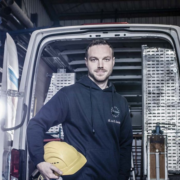 Ein Mann steht in einem Lieferwagen und hält einen gelben Helm, umgeben von Metallrohren in einem Lagerraum.