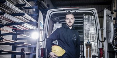 Ein Mann steht in einem Lieferwagen und hält einen gelben Helm, umgeben von Metallrohren in einem Lagerraum.