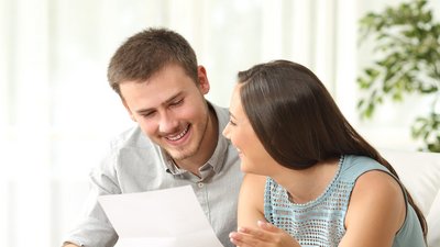 Ein Mann und eine Frau lachen sich an und halten ein Blatt in der Hand