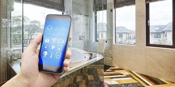 Badezimmer mit einer Hand die ein Smartphone hält, die eine Steuerung einer Lueftung-Klima-App zeigt.